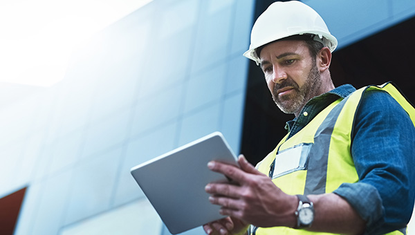 A man in construction vest in front of building looking at a tablet